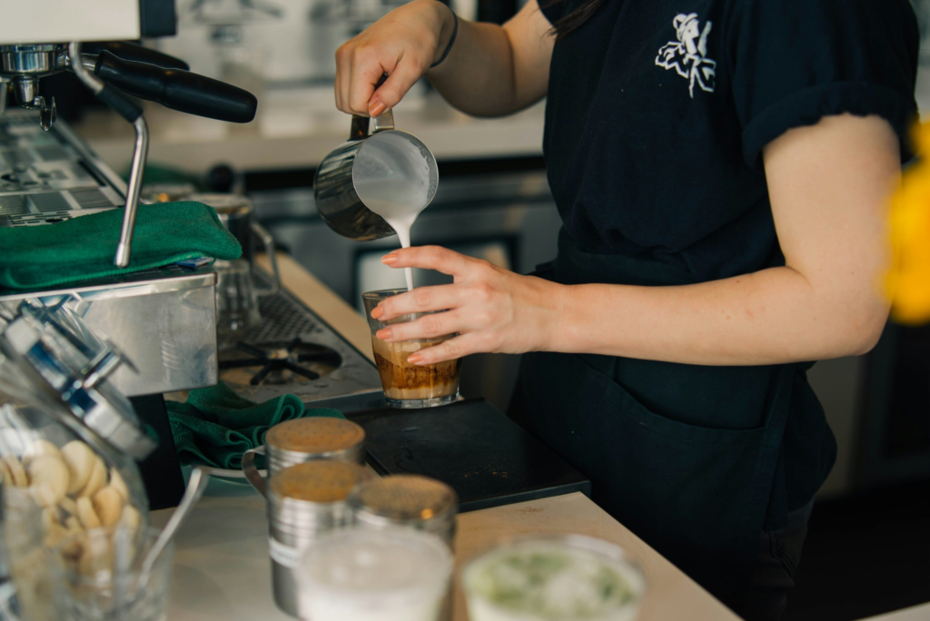 barista pours foam into a coffee cup behind a counter at a coffee shop