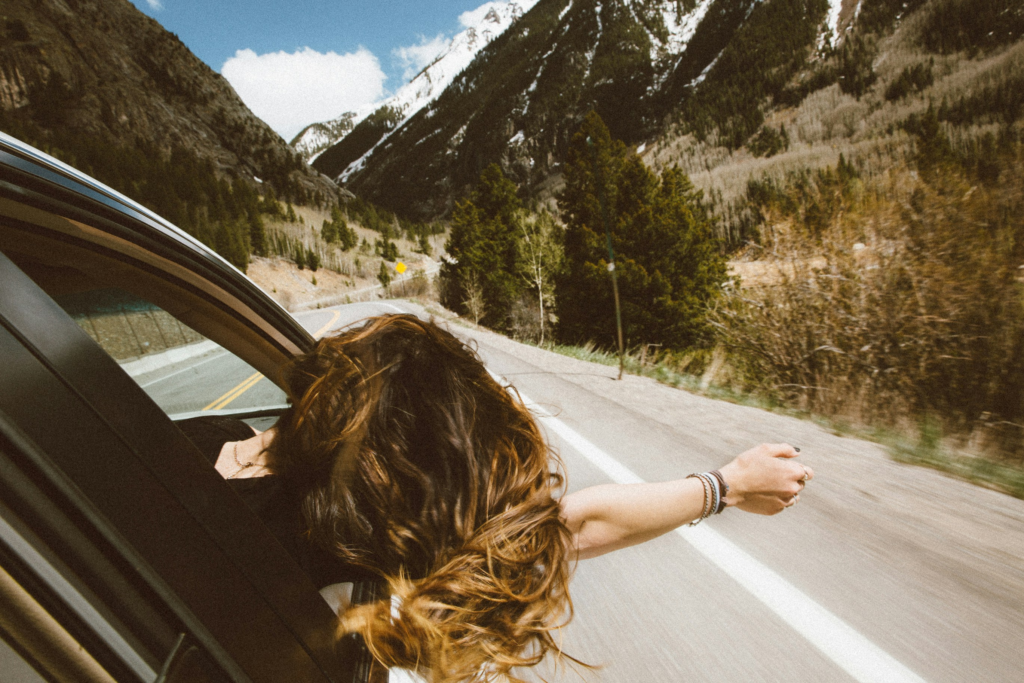 A women leaning out her car window while driving down a mountain road