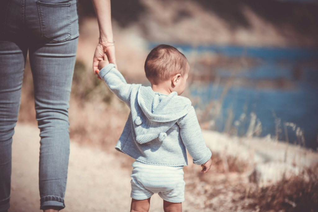 A child holds the hand of their Au Pair while walking along the lake