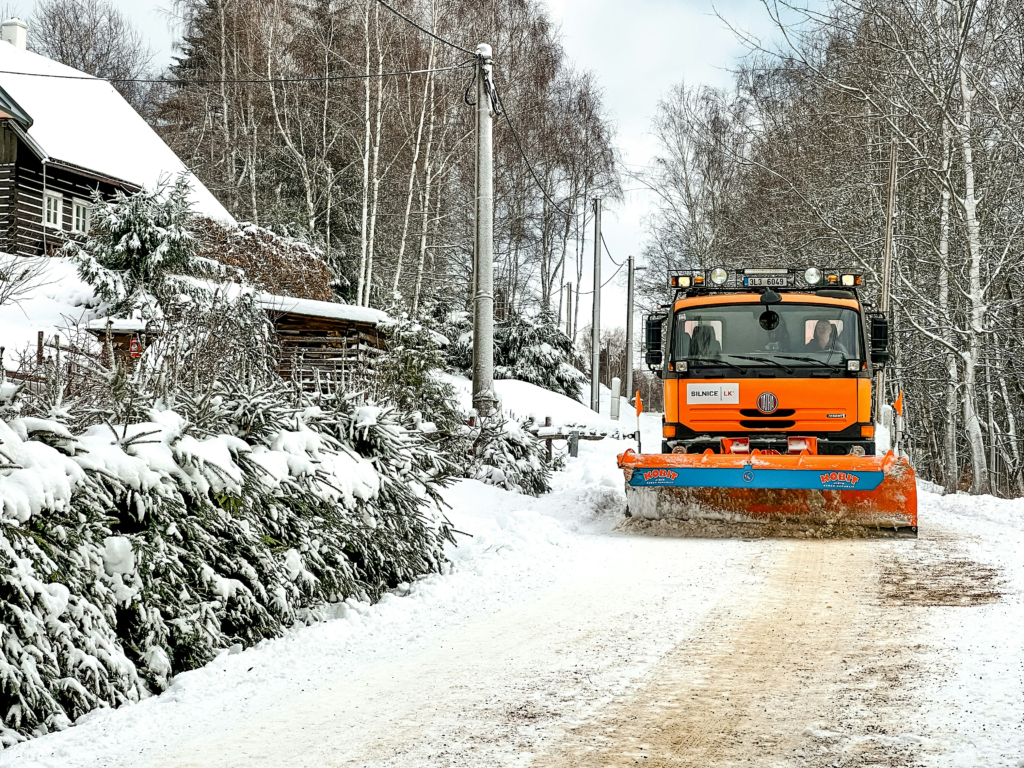 an orange snowplow clears a driveway of a snowy house in the woods