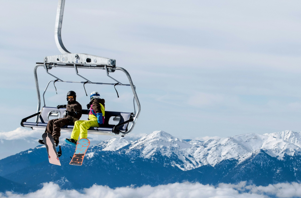 two snowboarders ride on a chair lift up a mountain