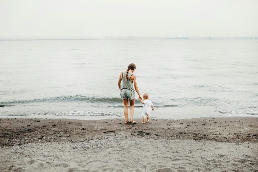 au pair holding her host childs hand and walking him down to the water at the beach