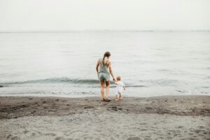 au pair holding her host childs hand and walking him down to the water at the beach