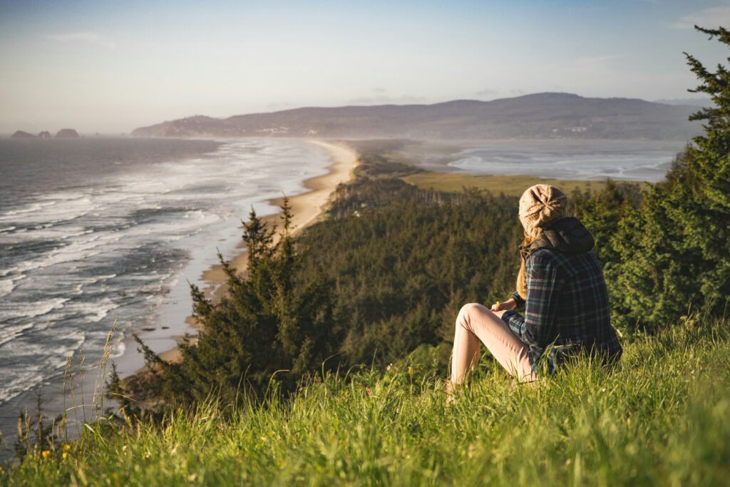 a girl sits on a grassy hill overlooking the ocean while living in another country