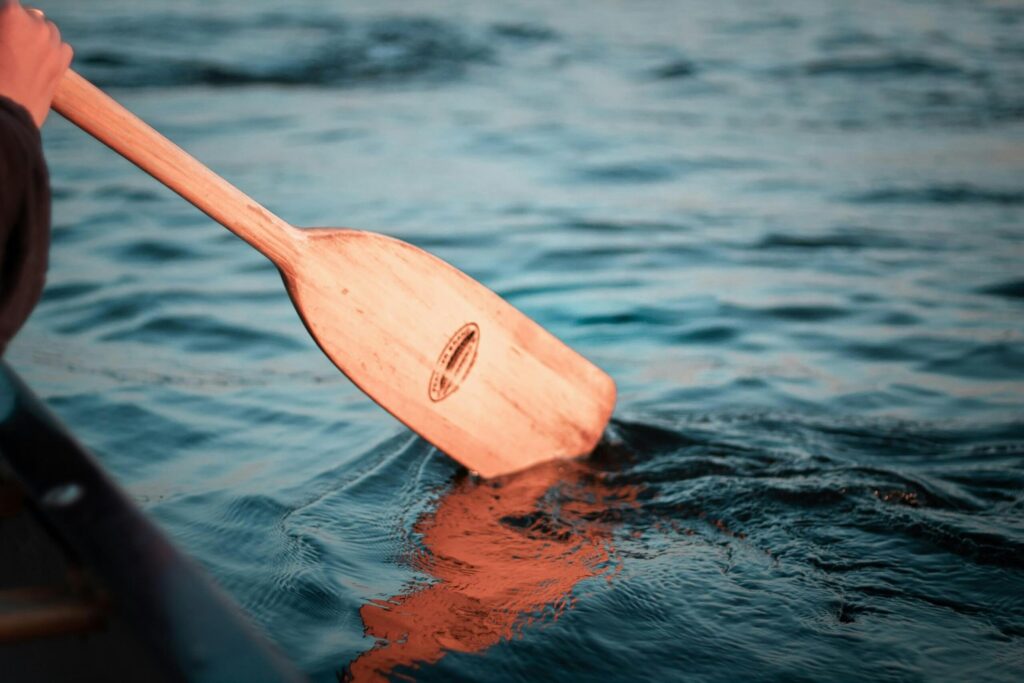 a wooden canoe paddle dips into the water