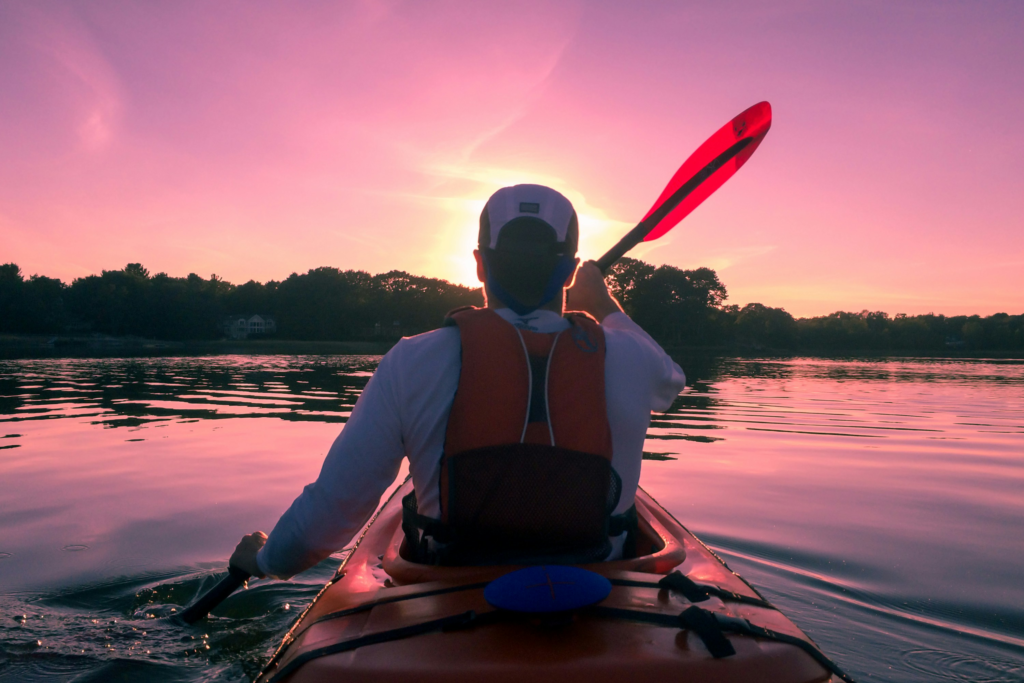 man paddles his kayak across a lake during sunset