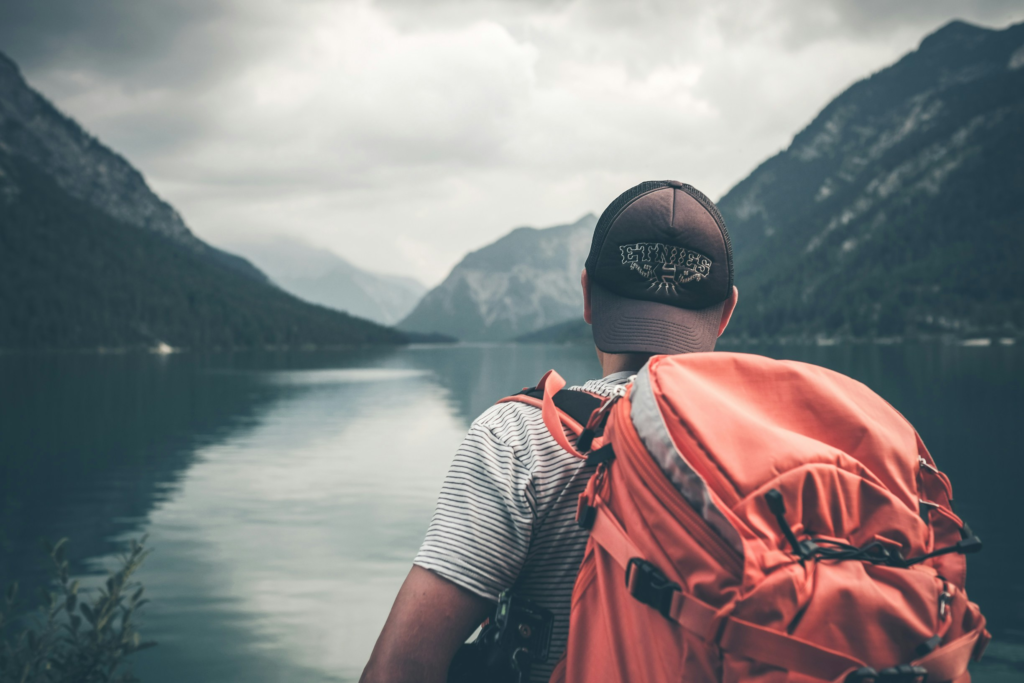 A man with a backpack gazes over a lake surrounded by mountains