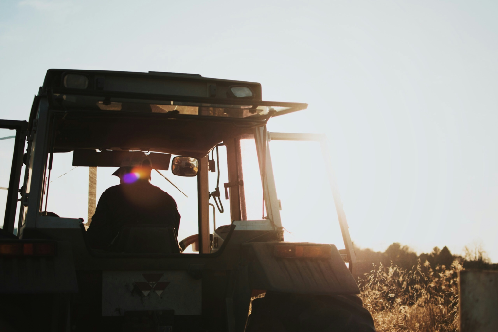 a ranch hand drives a tractor across a field as the sun sets
