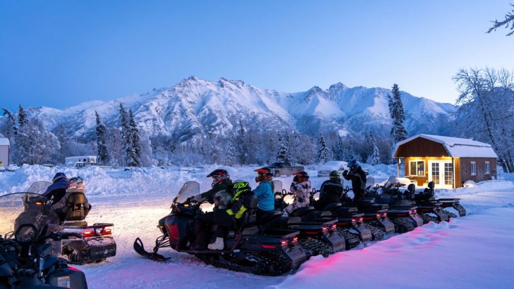 snowmobilers line up to ride under an alaskan winter sky