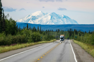 caravan driving down a road with Mount Denali in the background