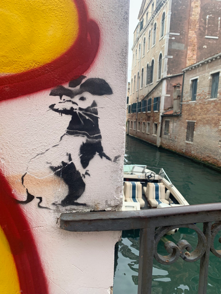street art in venice of a rad in a mask overlooking a canal