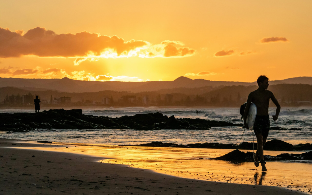 a surfer runs along the beach at sunset on the gold coast of Australia