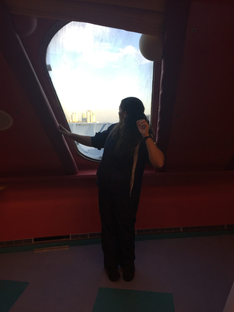 youth staff member looks out a port hole on a cruise ship