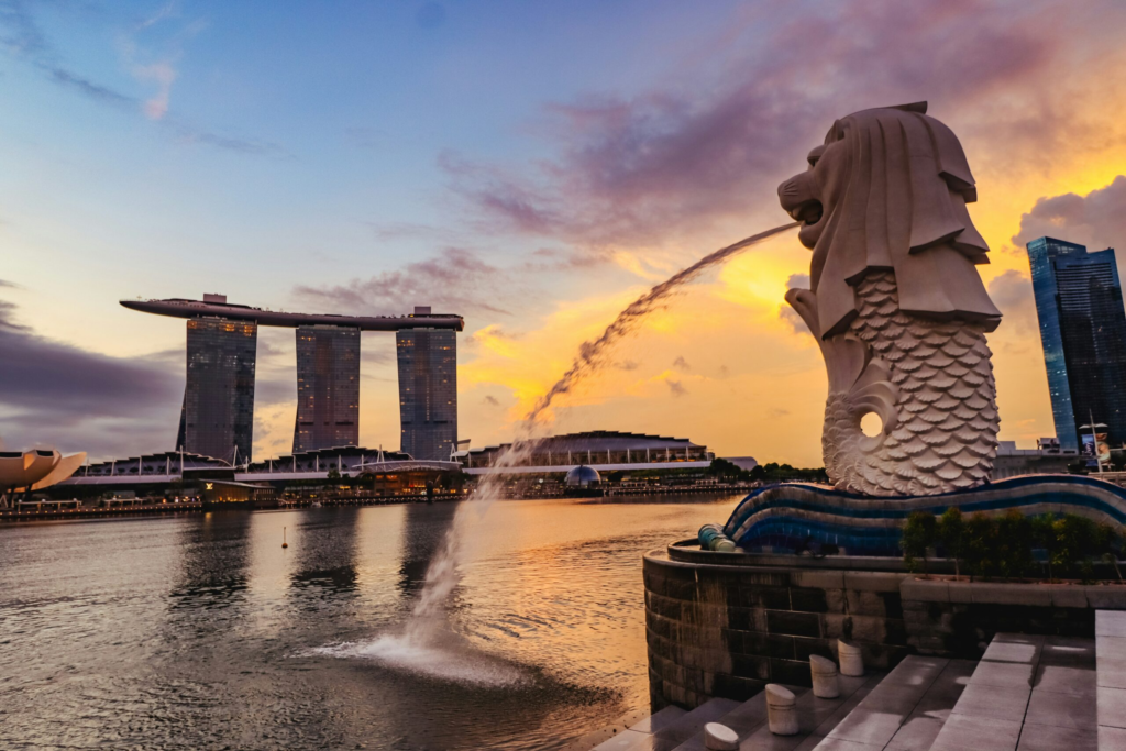 Singapore's famous Merlion statue sprays water into the pond while the sun sets over the city