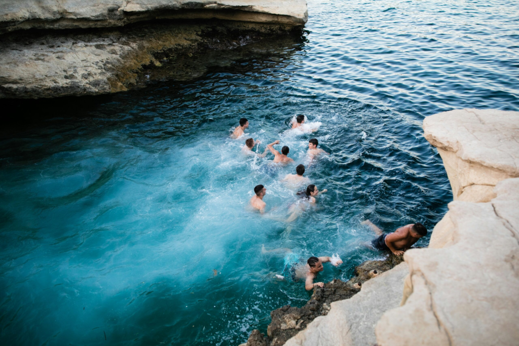 group of kids swimming in blue water between white rock cliffs