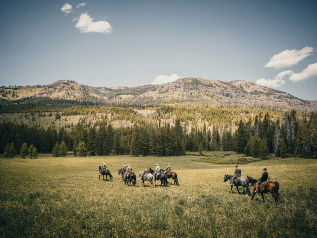 a cowboy takes a group of guest ranchers on a trail ride in an open field