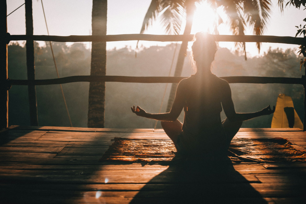 a women does yoga on a wooden balcony overlooking palms trees during sunrise
