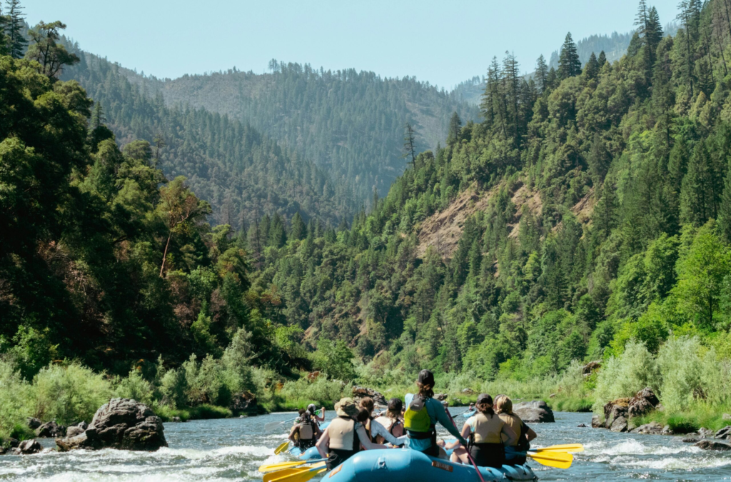 a raft guide paddles a group down a calm river that cuts through a green canyon